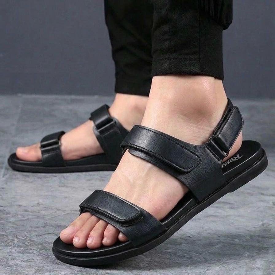 Black sandals worn with black pants on a gray floor.