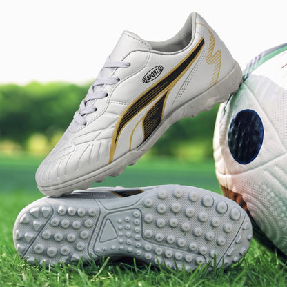 White Puma Sport turf soccer cleats with gold and black accents, shown on a green grass field next to a soccer ball.