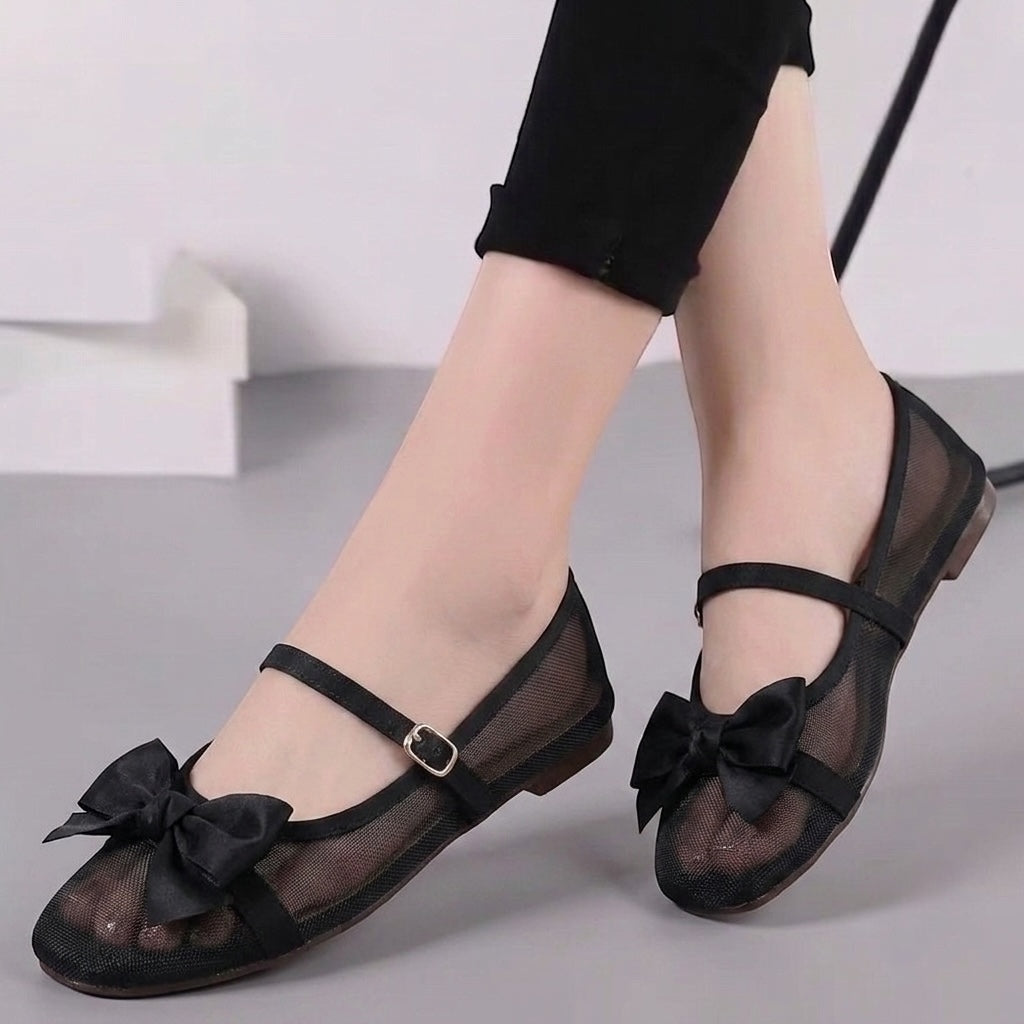 Black mesh flat shoes with bow details and ankle straps, shown on a model&