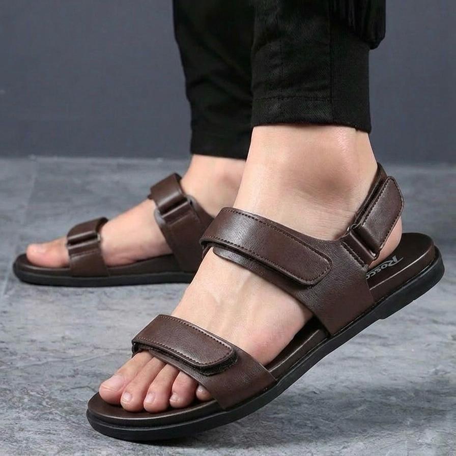 Brown sandals worn with black pants on a gray floor.