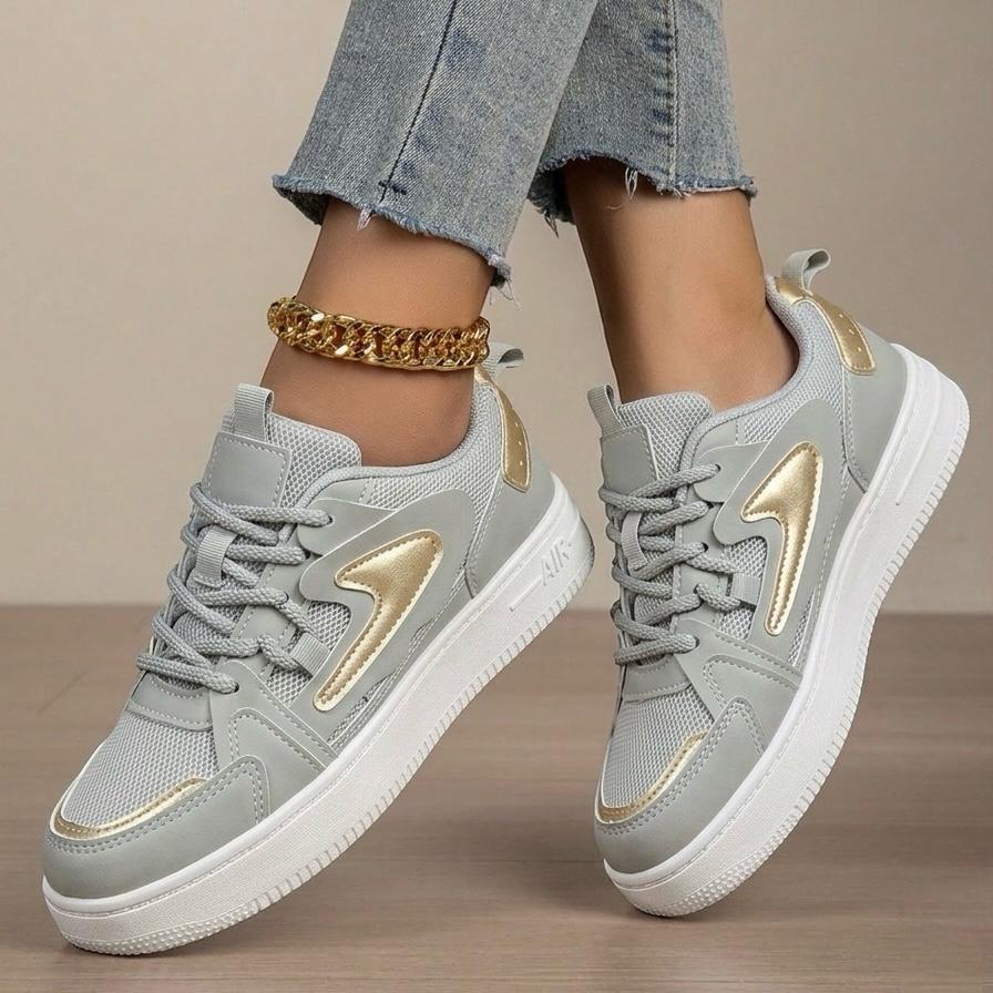Gray sneakers with gold accents worn by a person on a neutral background